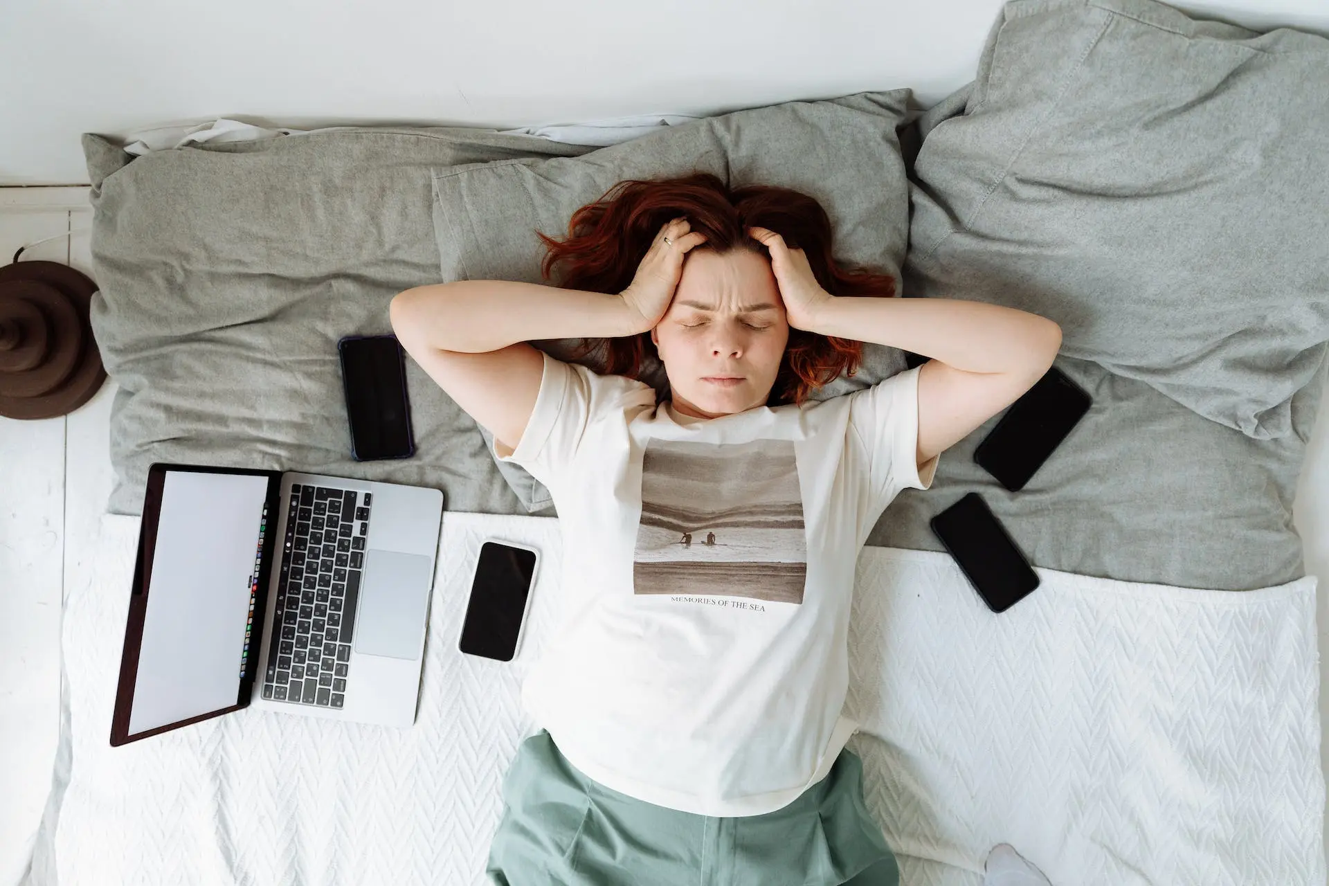 Woman surrounded by phones and laptop holding head